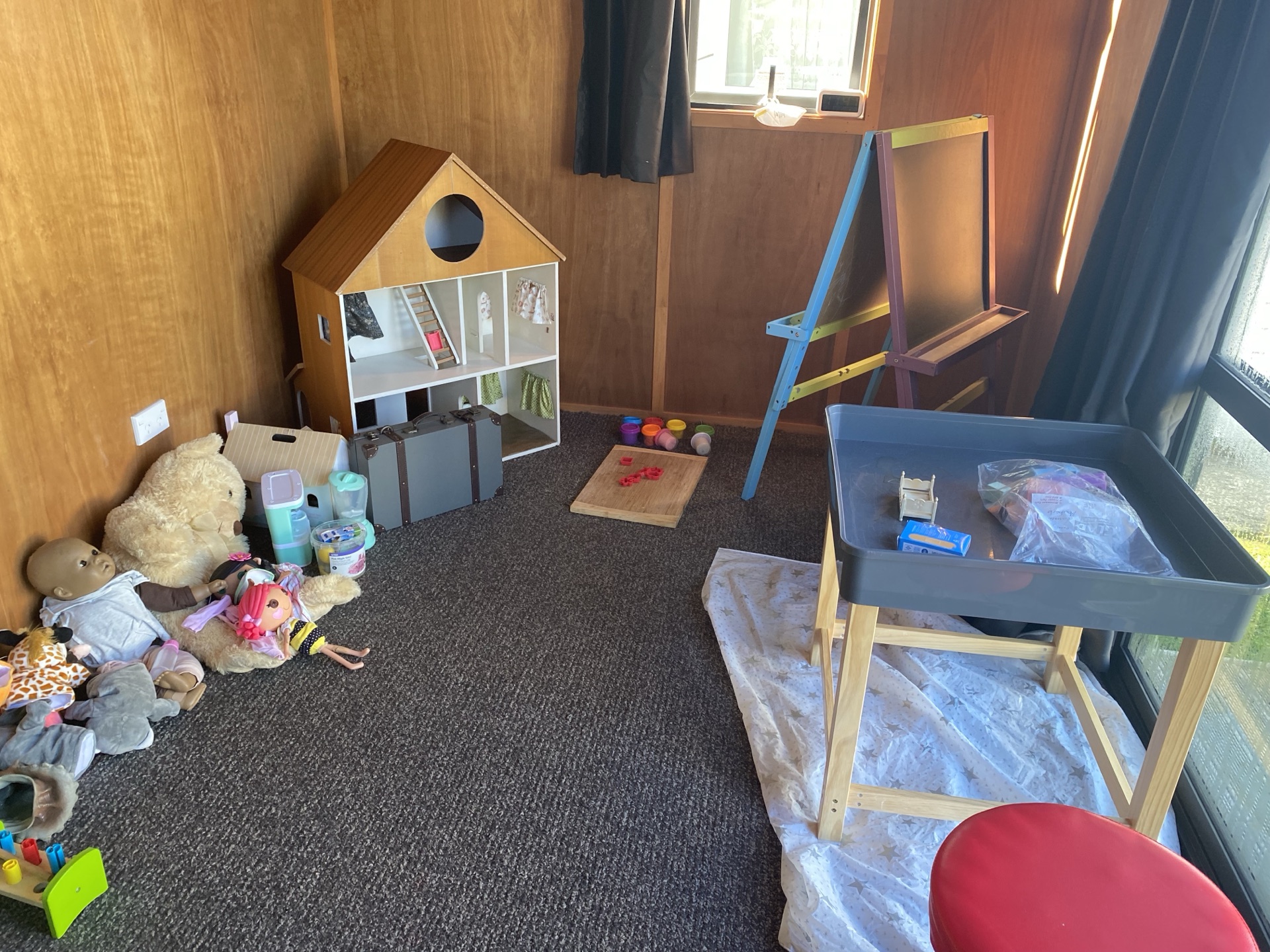 Playroom corner with a dollhouse, sand tray, easel and art materials
